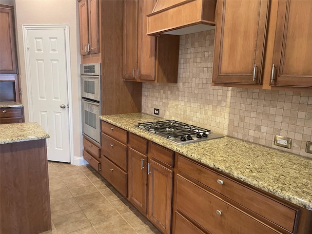 kitchen featuring appliances with stainless steel finishes, custom exhaust hood, light stone counters, and decorative backsplash