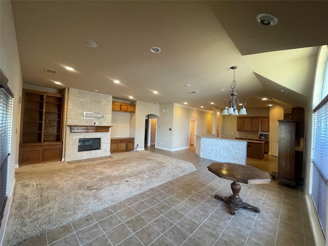 kitchen with arched walkways, light colored carpet, open floor plan, a center island, and a stone fireplace