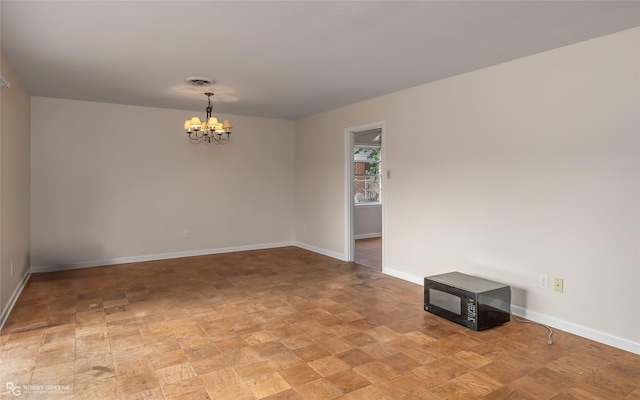 empty room featuring baseboards, visible vents, and a notable chandelier