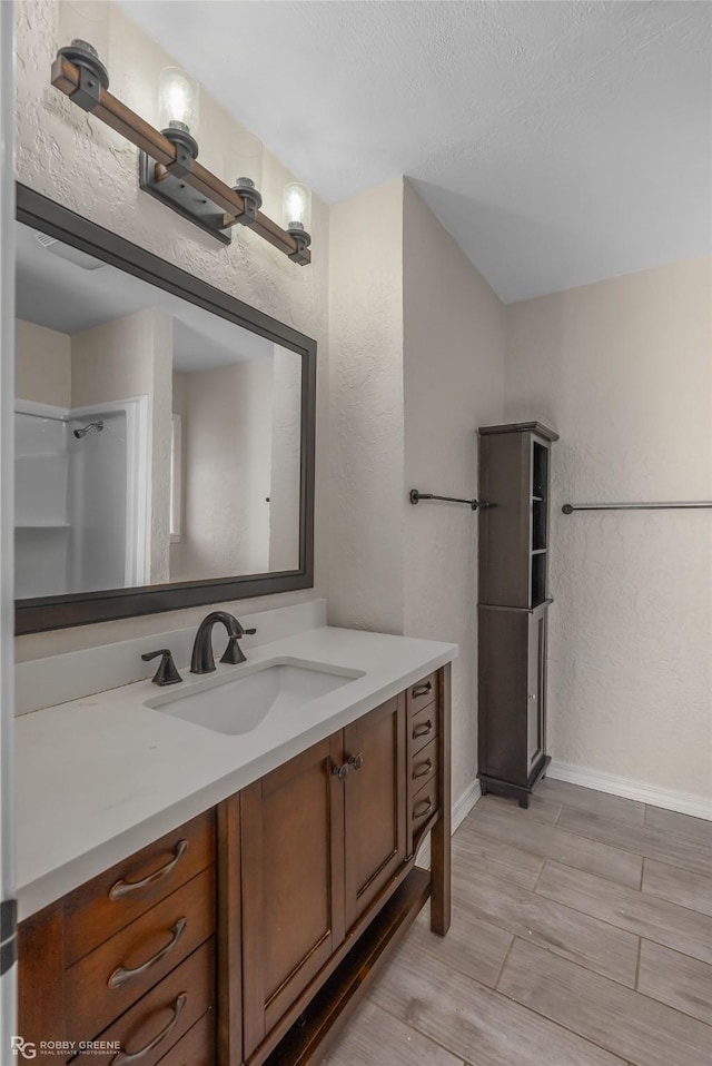 bathroom featuring wood finish floors, a textured wall, vanity, a textured ceiling, and baseboards