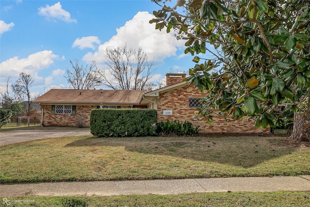 view of front of house with driveway, brick siding, a front lawn, and a chimney