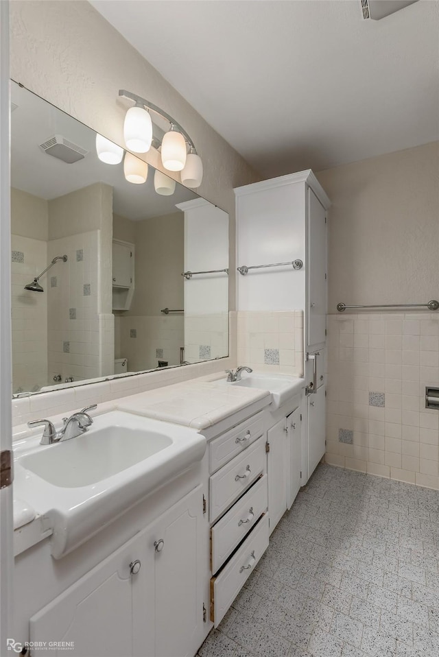 full bathroom with a sink, visible vents, tile walls, a shower stall, and double vanity