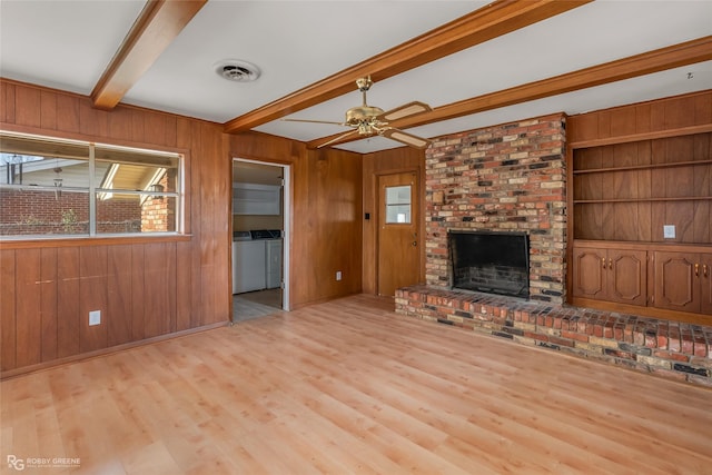 unfurnished living room with wooden walls, visible vents, a brick fireplace, beamed ceiling, and washing machine and clothes dryer