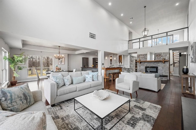 living room featuring a stone fireplace, dark wood-type flooring, visible vents, a tray ceiling, and an inviting chandelier