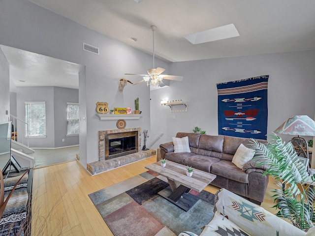 living room with visible vents, a glass covered fireplace, lofted ceiling with skylight, ceiling fan, and wood finished floors