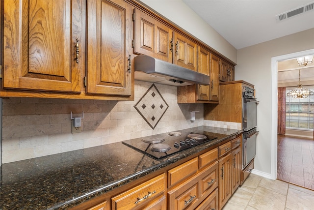 kitchen with brown cabinets, a notable chandelier, visible vents, under cabinet range hood, and black electric cooktop