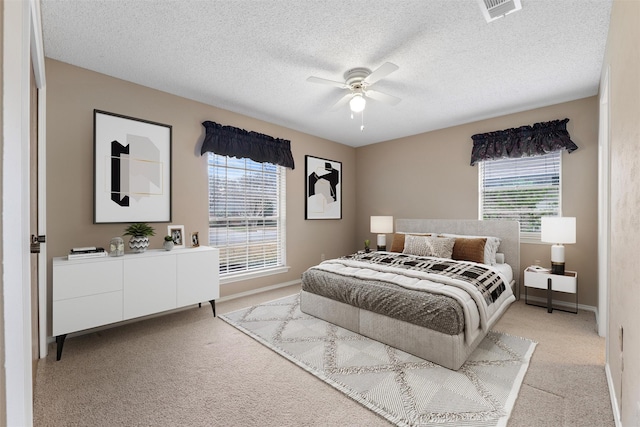 bedroom featuring baseboards, visible vents, a ceiling fan, light colored carpet, and a textured ceiling