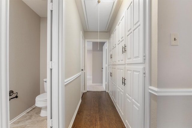 corridor featuring attic access, baseboards, and wood finished floors