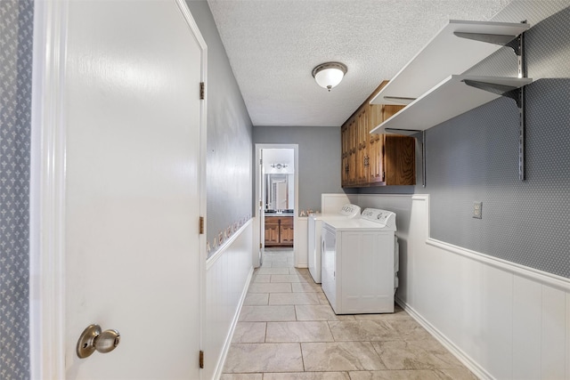 clothes washing area with washer and dryer, a wainscoted wall, cabinet space, and a textured ceiling