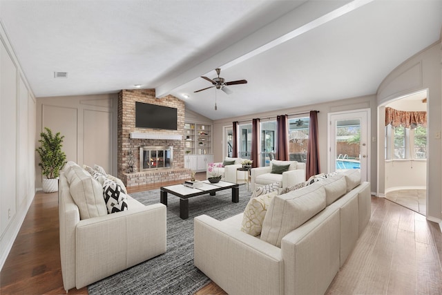 living room with vaulted ceiling with beams, visible vents, a decorative wall, a brick fireplace, and wood finished floors