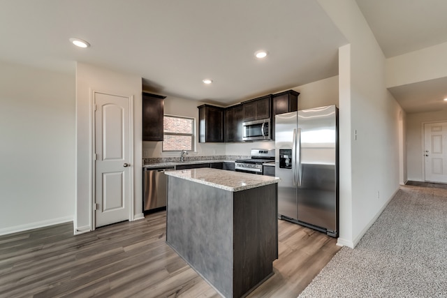 kitchen featuring a kitchen island, light stone counters, wood finished floors, stainless steel appliances, and dark brown cabinets