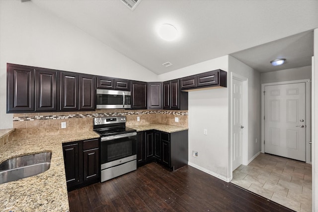 kitchen with appliances with stainless steel finishes, lofted ceiling, dark wood finished floors, and light stone countertops