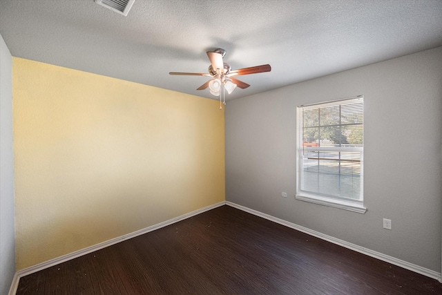 empty room featuring visible vents, dark wood finished floors, a textured ceiling, and baseboards