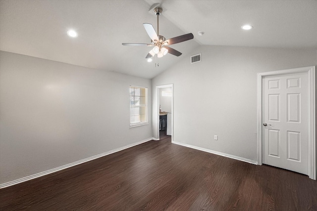 empty room with baseboards, visible vents, a ceiling fan, dark wood finished floors, and vaulted ceiling