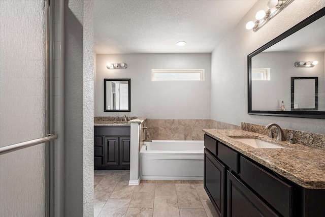 full bathroom with a garden tub, a textured ceiling, two vanities, and a sink