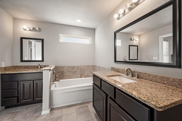 full bathroom featuring two vanities, a sink, a textured ceiling, and a bath