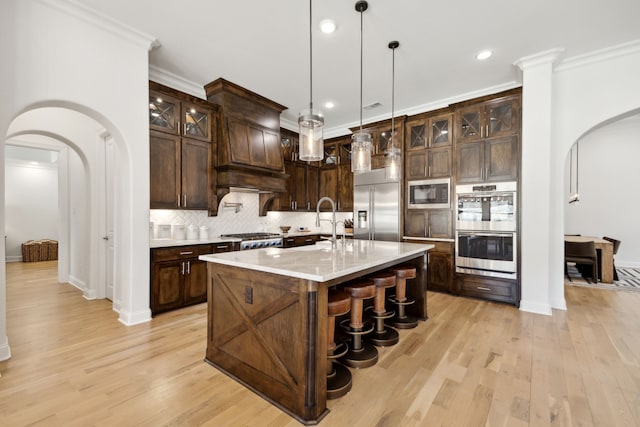 kitchen with light wood finished floors, arched walkways, decorative backsplash, and built in appliances