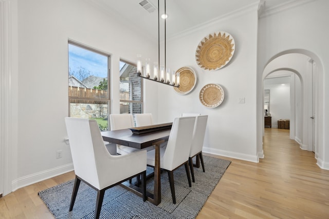 dining area with arched walkways, ornamental molding, visible vents, and light wood-style floors