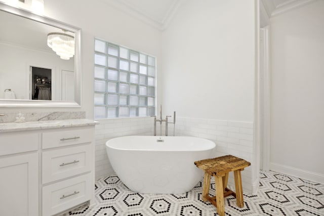 bathroom featuring a freestanding tub, tile walls, vanity, ornamental molding, and tile patterned floors