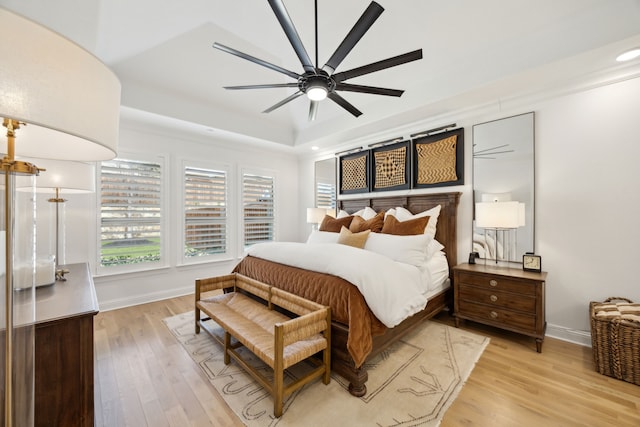 bedroom featuring ceiling fan, a raised ceiling, light wood-style flooring, and baseboards