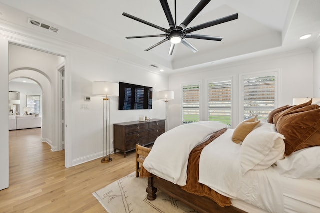 bedroom with light wood-type flooring, visible vents, a raised ceiling, and arched walkways