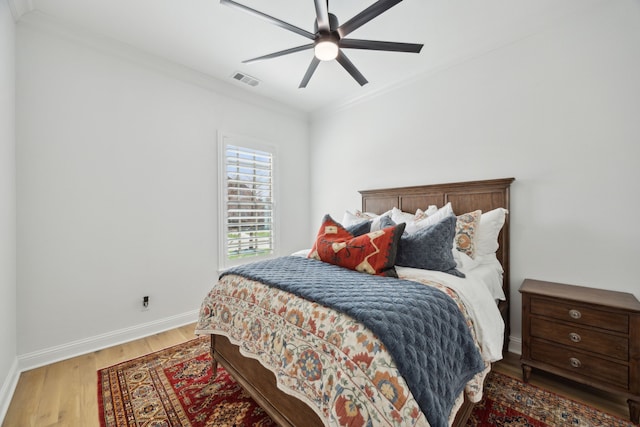 bedroom with wood finished floors, a ceiling fan, visible vents, baseboards, and ornamental molding