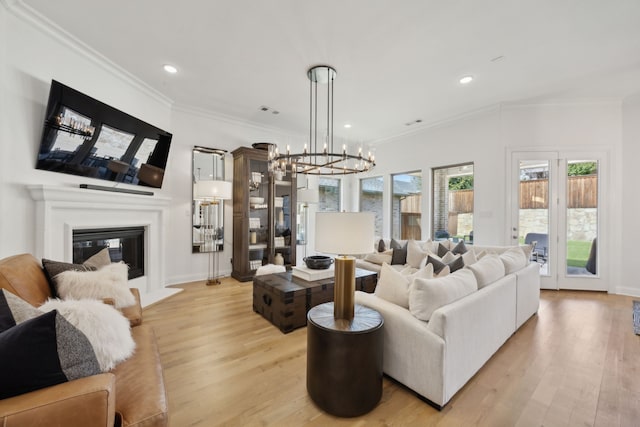 living area with light wood-style floors, recessed lighting, crown molding, and a glass covered fireplace