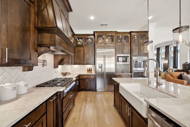 kitchen with tasteful backsplash, visible vents, glass insert cabinets, a sink, and built in appliances