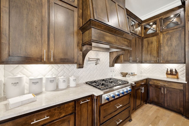 kitchen featuring tasteful backsplash, stainless steel gas stovetop, light wood-style floors, glass insert cabinets, and dark brown cabinetry