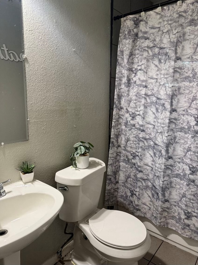 bathroom featuring a textured wall, toilet, curtained shower, tile patterned flooring, and a sink