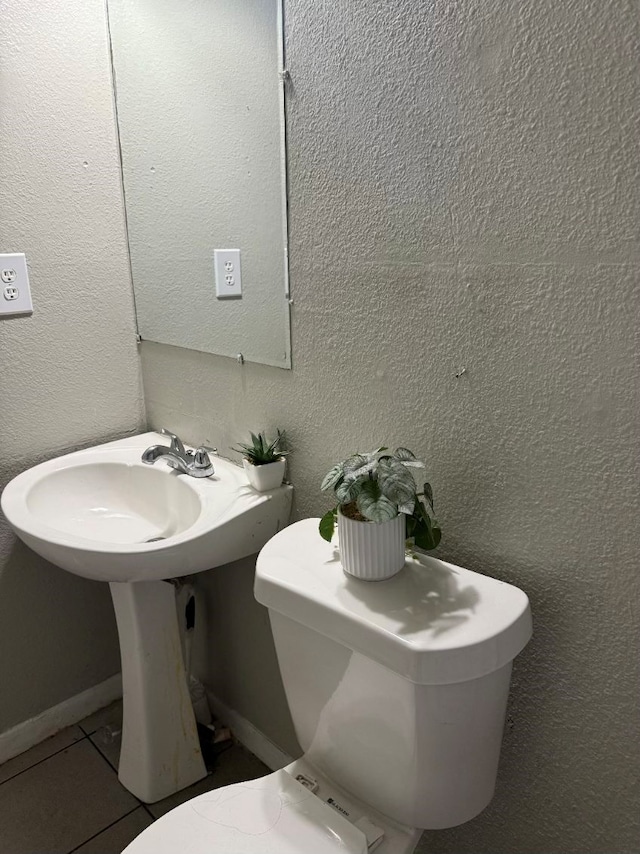 bathroom featuring baseboards, a textured wall, toilet, and tile patterned floors