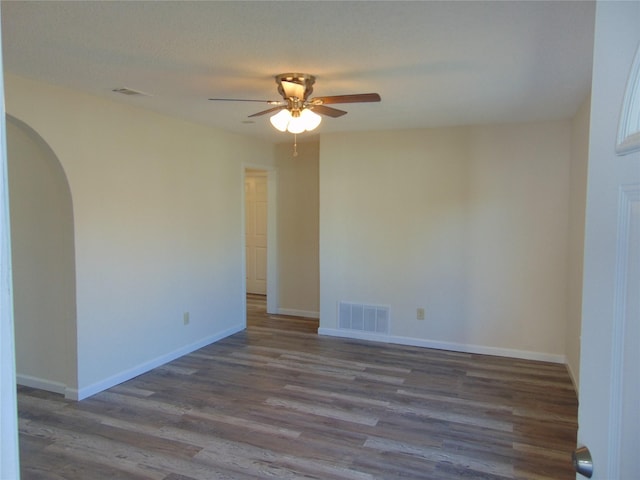 spare room with arched walkways, visible vents, baseboards, and wood finished floors