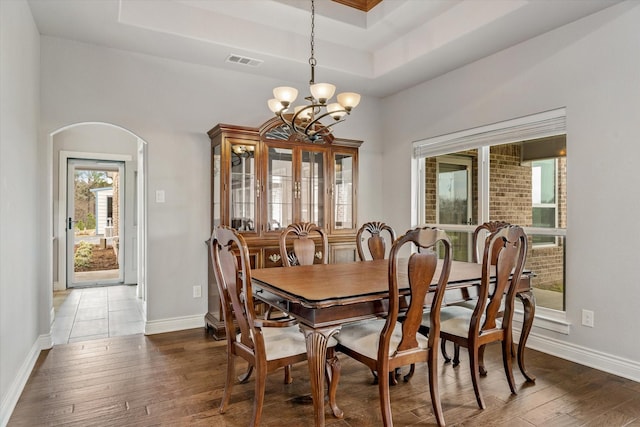 dining space featuring arched walkways, visible vents, a raised ceiling, and hardwood / wood-style floors