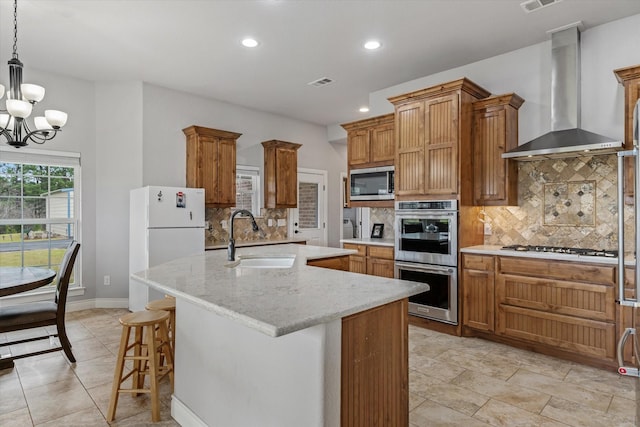 kitchen featuring brown cabinets, wall chimney range hood, stainless steel appliances, and a sink