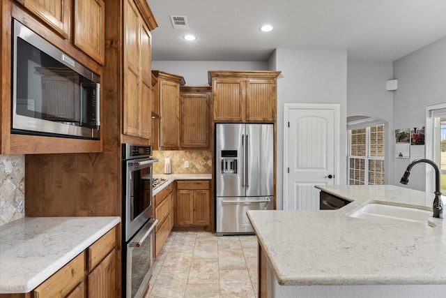 kitchen with brown cabinets, stainless steel appliances, visible vents, decorative backsplash, and a sink