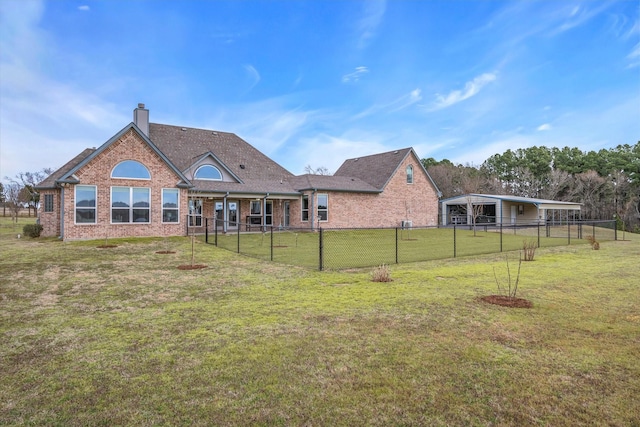 rear view of house featuring brick siding, a chimney, a lawn, a carport, and a fenced backyard