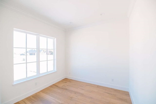 empty room with crown molding, light wood-style flooring, and baseboards