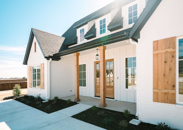 view of exterior entry featuring board and batten siding, covered porch, brick siding, and a shingled roof