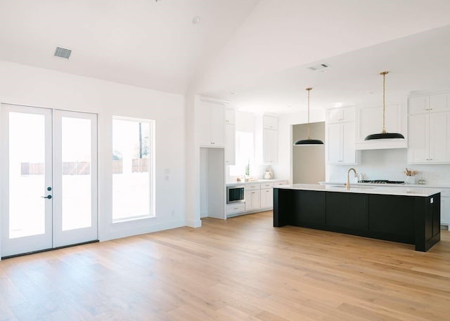 kitchen featuring visible vents, white cabinets, an island with sink, light countertops, and light wood-type flooring