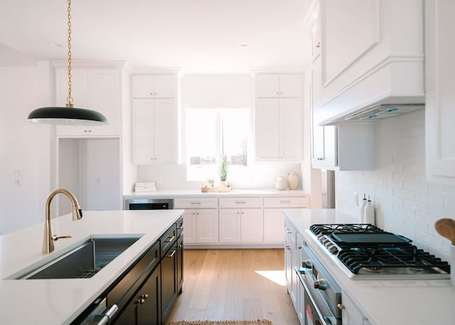 kitchen with stainless steel appliances, premium range hood, a sink, white cabinetry, and decorative light fixtures