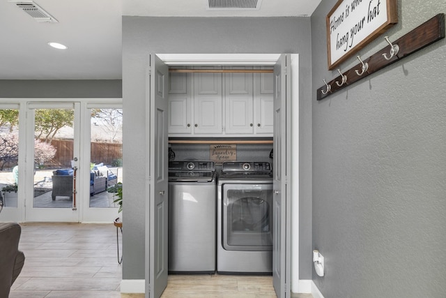 laundry area featuring visible vents, a textured wall, cabinet space, and washer and dryer