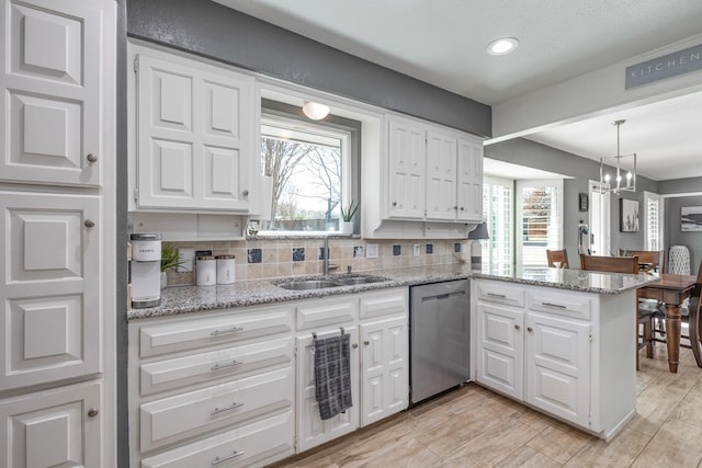 kitchen featuring a peninsula, a sink, white cabinetry, dishwasher, and tasteful backsplash