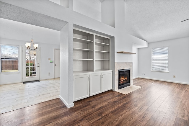 unfurnished living room with a textured ceiling, a chandelier, wood finished floors, a fireplace with flush hearth, and baseboards