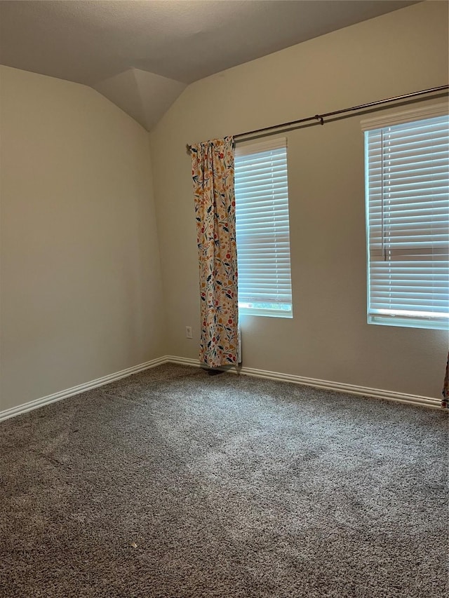 carpeted empty room with a healthy amount of sunlight, vaulted ceiling, and baseboards