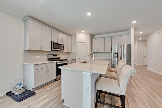 6116 Pathfinder Trl, Fort Worth, TX 76179 - kitchen with appliances with stainless steel finishes, a sink, light wood-style floors, decorative backsplash, and a kitchen breakfast bar