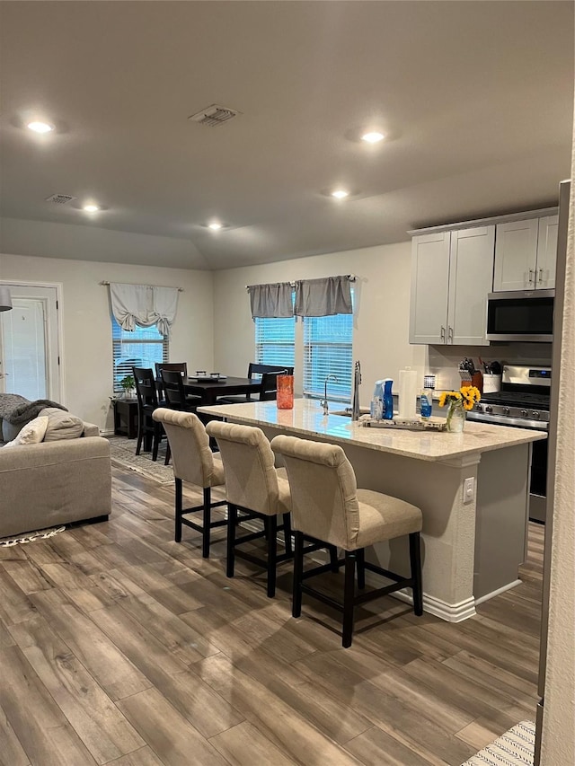 kitchen with appliances with stainless steel finishes, dark wood-style flooring, visible vents, and a kitchen breakfast bar