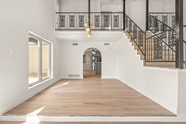 entryway with a towering ceiling, visible vents, arched walkways, and wood finished floors