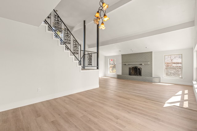 unfurnished living room featuring baseboards, light wood-style flooring, stairway, a fireplace, and a chandelier