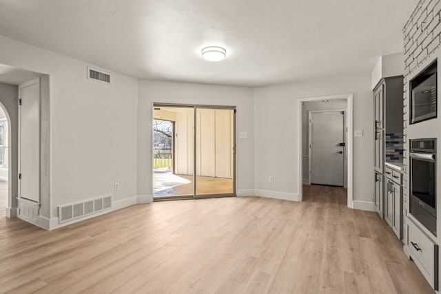 unfurnished living room with light wood-style flooring, visible vents, and baseboards