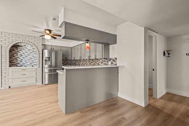 kitchen with light wood finished floors, light countertops, gray cabinetry, stainless steel fridge, and a peninsula